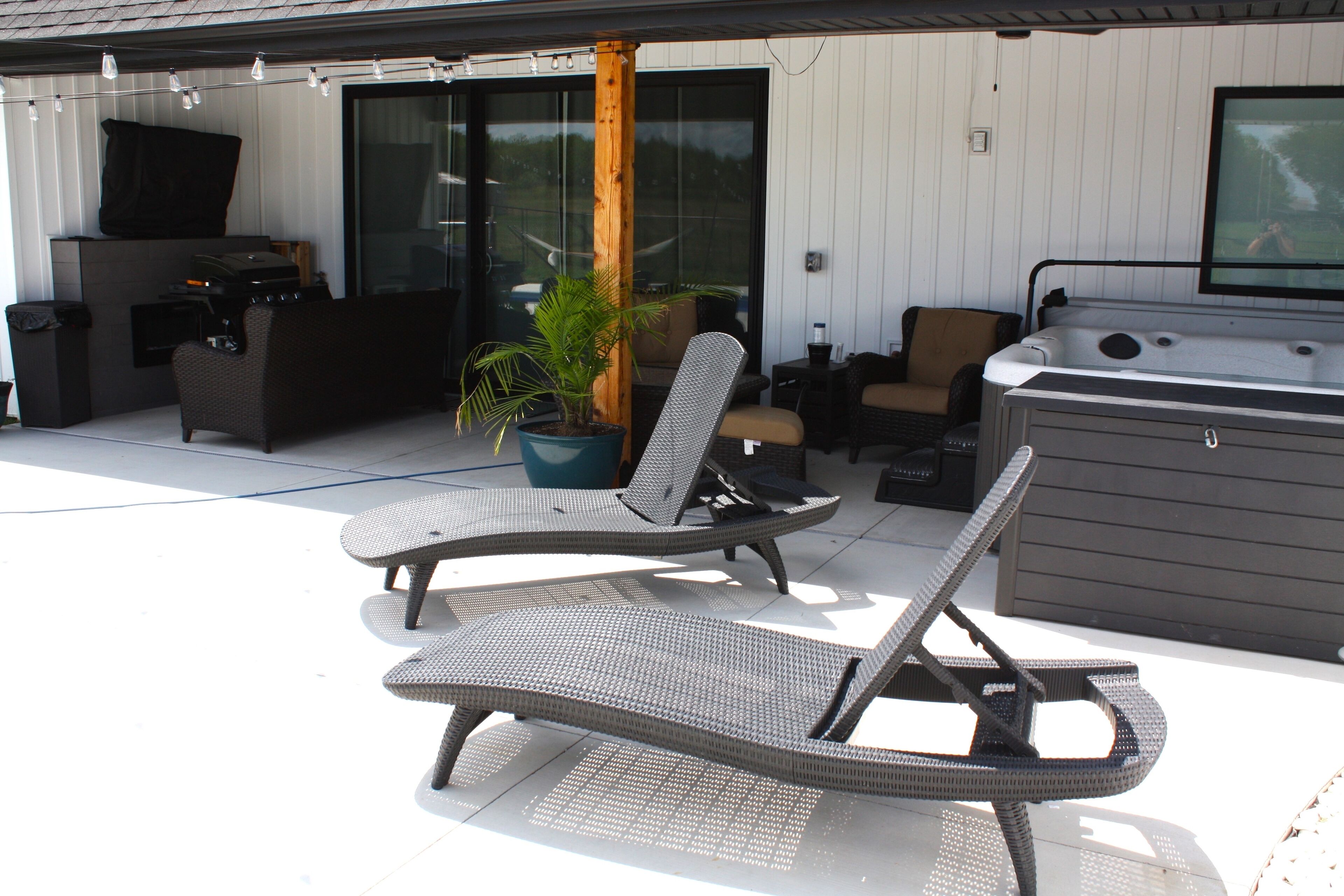 Un patio al aire libre con sillones de mimbre, un jacuzzi y una planta en maceta.