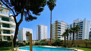 Une piscine entourée de pelouse bien entretenue et de palmiers, avec des bâtiments modernes en arrière-plan.