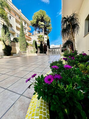 A courtyard with tiled flooring, a central tree, and purple flowers. - 2 Bedroom Apartment in Puerto Marina (Benalmádena)