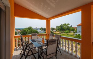 A balcony with a table and chairs, offering a view of a residential area with houses and greenery.