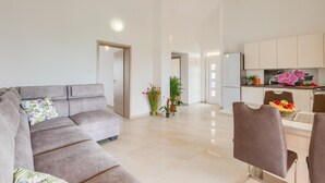 A modern living room with a grey sofa, a dining area with a table and chairs, and a kitchen with white cabinets and a refrigerator. - Luxurious home in Vodnjan (Vodnjan)