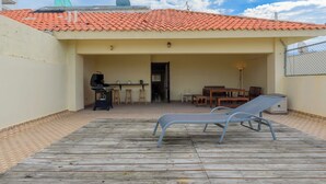 A covered outdoor area with a wooden deck, a barbecue grill, and a seating area with tables and chairs. -  Penthouse in Evaristo Morales Sleeps 14 (Santo Domingo)