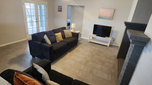 A living room with a dark sofa, a flat-screen TV, a fireplace, and a door leading to a balcony.