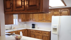 A kitchen with wooden cabinets, a white countertop, a coffee maker, and a refrigerator.