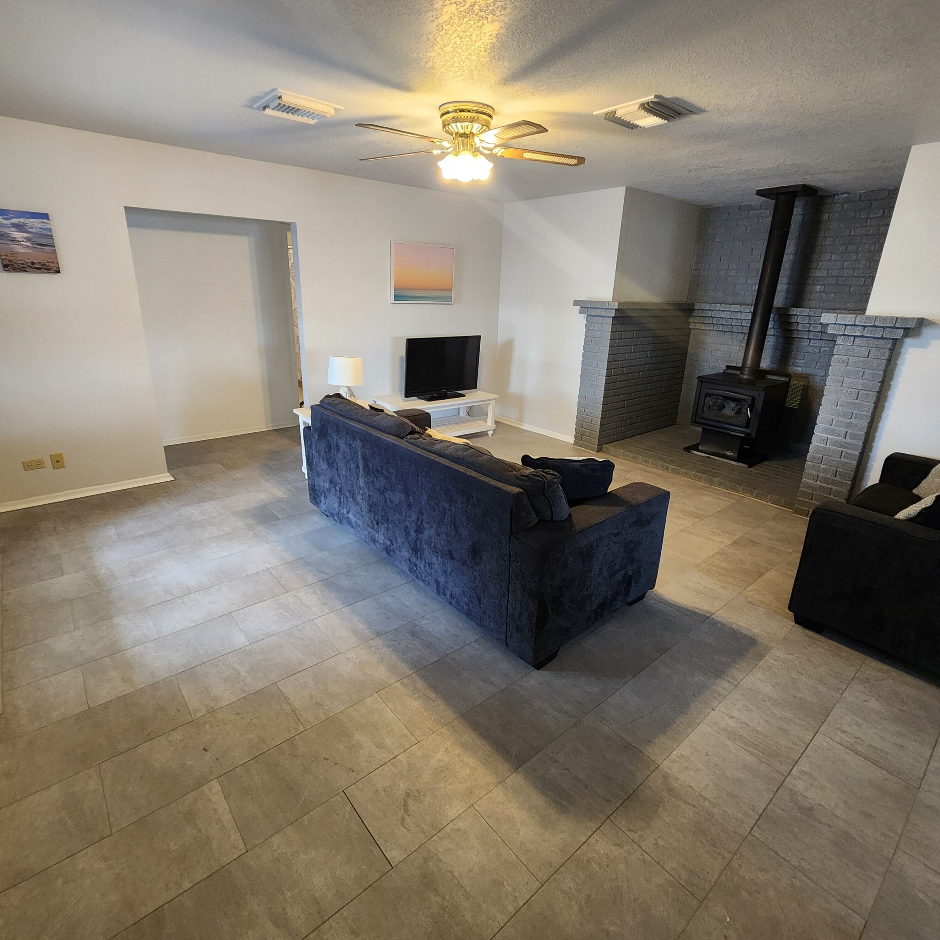 A spacious living room with a dark blue sofa, a flat-screen TV, a fireplace, and a ceiling fan.