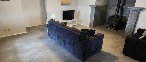 A spacious living room with a dark blue sofa, a flat-screen TV, a fireplace, and a ceiling fan.
