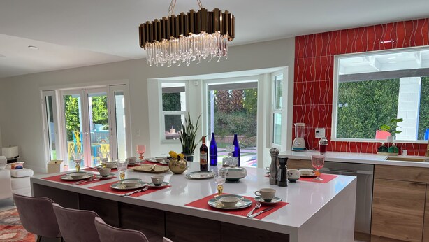 Eine moderne Küche mit einer zentralen Kochinsel, Barhocker und einer roten Spritzschutzwand.