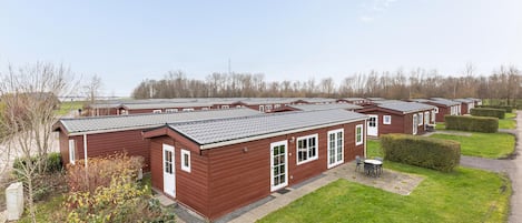 A row of red wooden mobile homes with grey roofs, arranged in a neat row with green lawns and trimmed bushes in front.