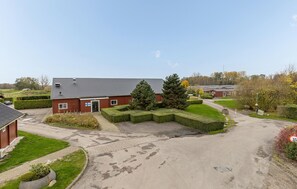 A red brick building with a grey roof, surrounded by well-maintained hedges and a paved driveway.