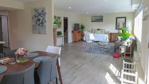 A spacious living area with a dining table, chairs, a sofa, and a coffee table. There is a staircase leading to an upper level.