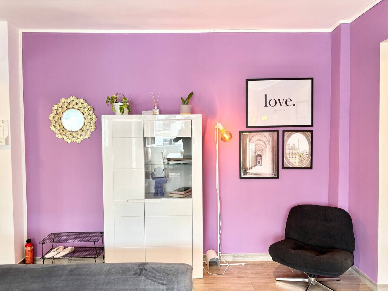 A room with a purple wall, a white cabinet, a black chair, and a framed picture with the word 'love.'