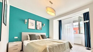 Een slaapkamer met een bed, nachtkastje, een wandlamp en een raam met gordijnen.