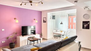 Een moderne woonkamer met een bank, televisie en een eethoek.