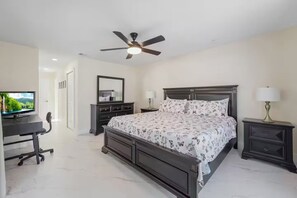 A bedroom with a bed, a desk, a television, a ceiling fan, and a nightstand.