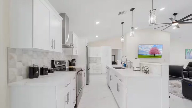 Une cuisine moderne avec des meubles blancs, des appareils en acier inoxydable et des luminaires suspendus.