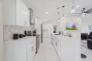 A modern kitchen with white cabinetry, stainless steel appliances, and pendant lighting. - Home with heated pool and a pool table in Cape Coral (Cape Coral)