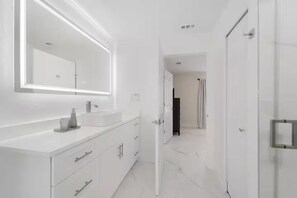 A modern bathroom with a large mirror, white vanity, and a door leading to another room.