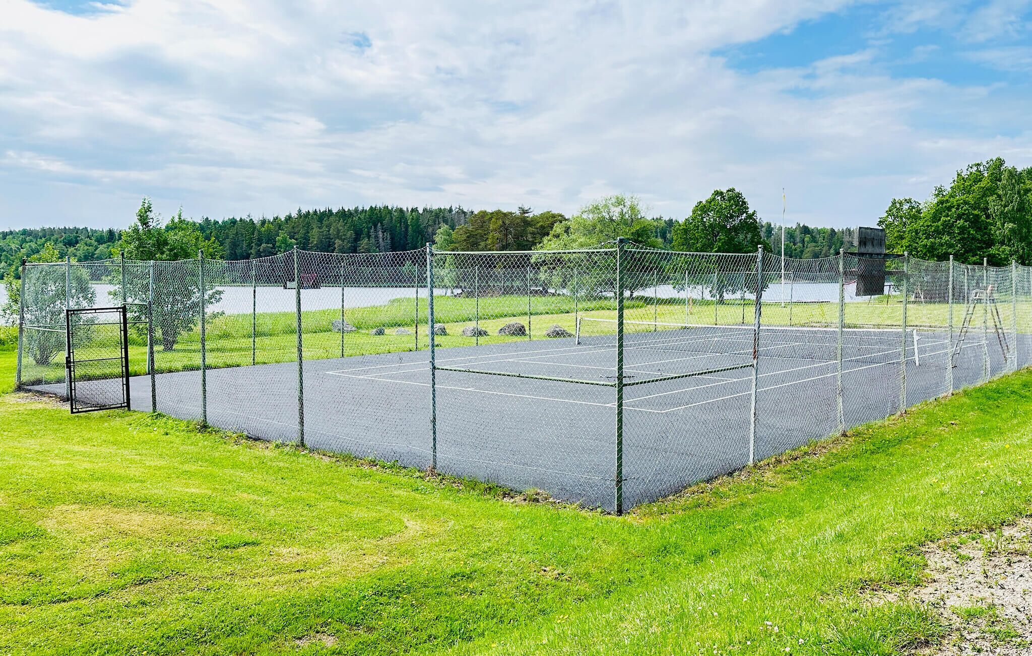 A fenced tennis court with a net, surrounded by grass and trees.