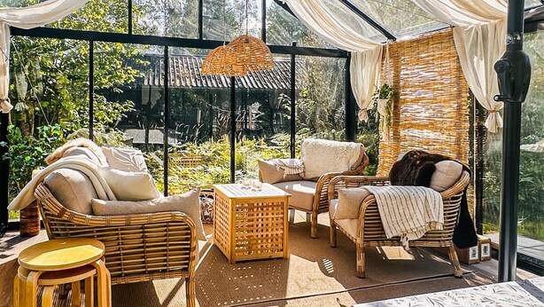A conservatory with wicker furniture, a woven ceiling, and a view of greenery.