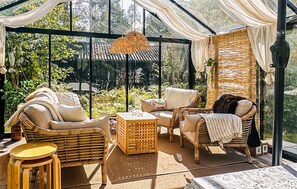 Ein Wintergarten mit Korbmöbeln, einer gewebten Decke und Blick auf Grünflächen.