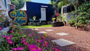 Un jardín con un mural colorido, una zona de estar con mesa y sillas, y plantas en macetas.