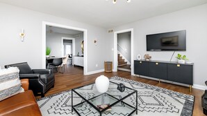 Un salon moderne avec une table basse en verre, un canapé en cuir noir, un tapis noir et blanc, un meuble TV noir et un escalier menant à une autre pièce.