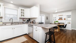 Une cuisine moderne avec des meubles blancs, un plan de travail en marbre et un coin repas comprenant une table en bois et des chaises noires.