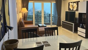 Ein modernes Wohnzimmer mit einer Couch, einem Esstisch und Stühlen. Ein Balkon bietet Blick auf die Stadt.