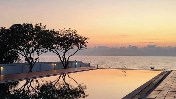 Ein ruhiger Poolbereich am Wasser mit einem Baum und einem klaren Blick auf das Meer bei Sonnenuntergang.