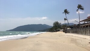 Ein Strand mit einer Holzlattenzaun, Palmen und einem Berg im Hintergrund.