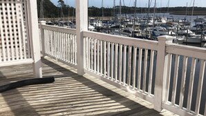 Eine Holzterrasse mit weißer Reling, die auf einen Yachthafen mit mehreren Booten blickt.