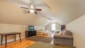 Ein geräumiger Lofts mit hohen Decken, zwei Deckenventilatoren, einem großen Fenster, einem Flachbildfernseher, einer Couch, einem Couchtisch und einem kleinen Tisch.