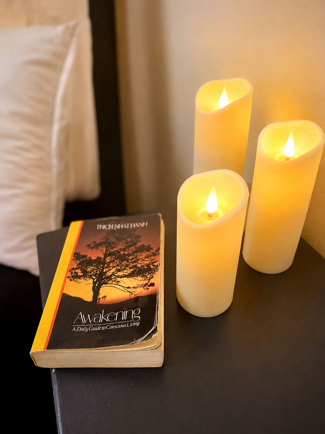 A book titled 'Awakening' next to three lit candles on a table.