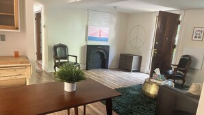 A living room with a wooden table, a green rug, a fireplace, and a painting of a bridge.