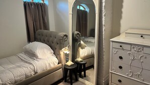 A bedroom with a bed, a dresser, a mirror, and a window with curtains.