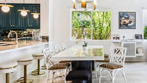 Een moderne keuken met een centraal eiland, hangende verlichting en een groot raam met uitzicht op groen.