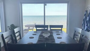 Un comedor con una mesa y sillas, vista al océano a través de amplios ventanales y un respiradero en el techo.