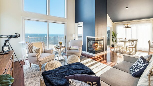 Amplia sala de estar con un ventanal con vistas al mar, chimenea y comedor.