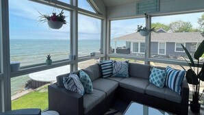 Un solárium con un gran ventanal con vistas al océano, un sofá modular gris con cojines estampados y una mesa de centro de vidrio.