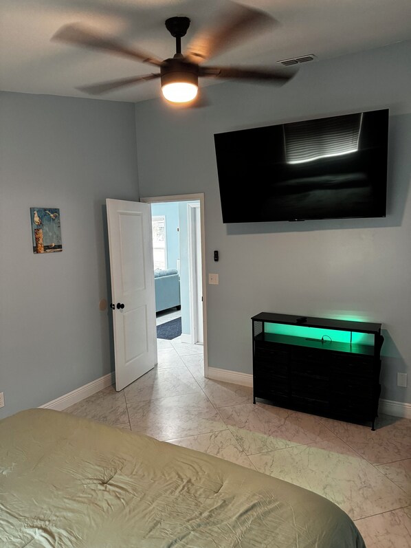 A bedroom with a bed, a ceiling fan, a TV, and a dresser.