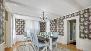 Ein Esszimmer mit einem Holztisch, sechs blau gepolsterten Stühlen, einer Kristallleuchtre und blumigem Wandpapier.