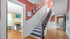 Eine Treppe mit weißer Wand und rotem Zierstreifen, die zu einem Raum mit Kamin und Essbereich führt.