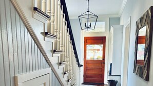A hallway with a wooden staircase, a wooden door at the end, and a patterned rug on the floor.