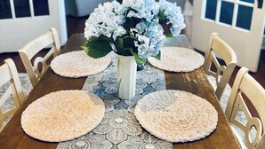 A dining table with a vase of flowers, placemats, and chairs in a room with a view of a living area.