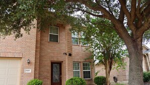 A two-story brick house with a garage, a front door with a decorative glass panel, and a small front yard with trimmed bushes and a tree. - Spacious & Stylish, Two-Story Home Near Willowbrook Mall. (Houston)
