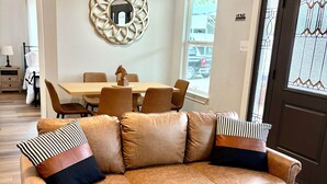 A living room with a brown leather sofa, a wooden coffee table, and a dining area with a wooden table and chairs. - Cielo’s Retreat, A Charming 3-bedroom farmhouse in McKinneyprincenton (McKinney)