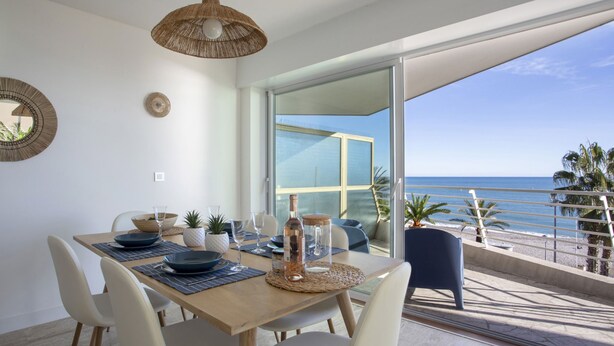 A dining area with a view of the ocean, a large window, and a balcony with a railing. - Le Chantilly by Interhome (Cagnes-sur-Mer)