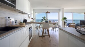 A modern kitchen with a view of the sea, featuring white cabinetry, wooden flooring, and a dining area with a view. - Le Chantilly by Interhome (Cagnes-sur-Mer)