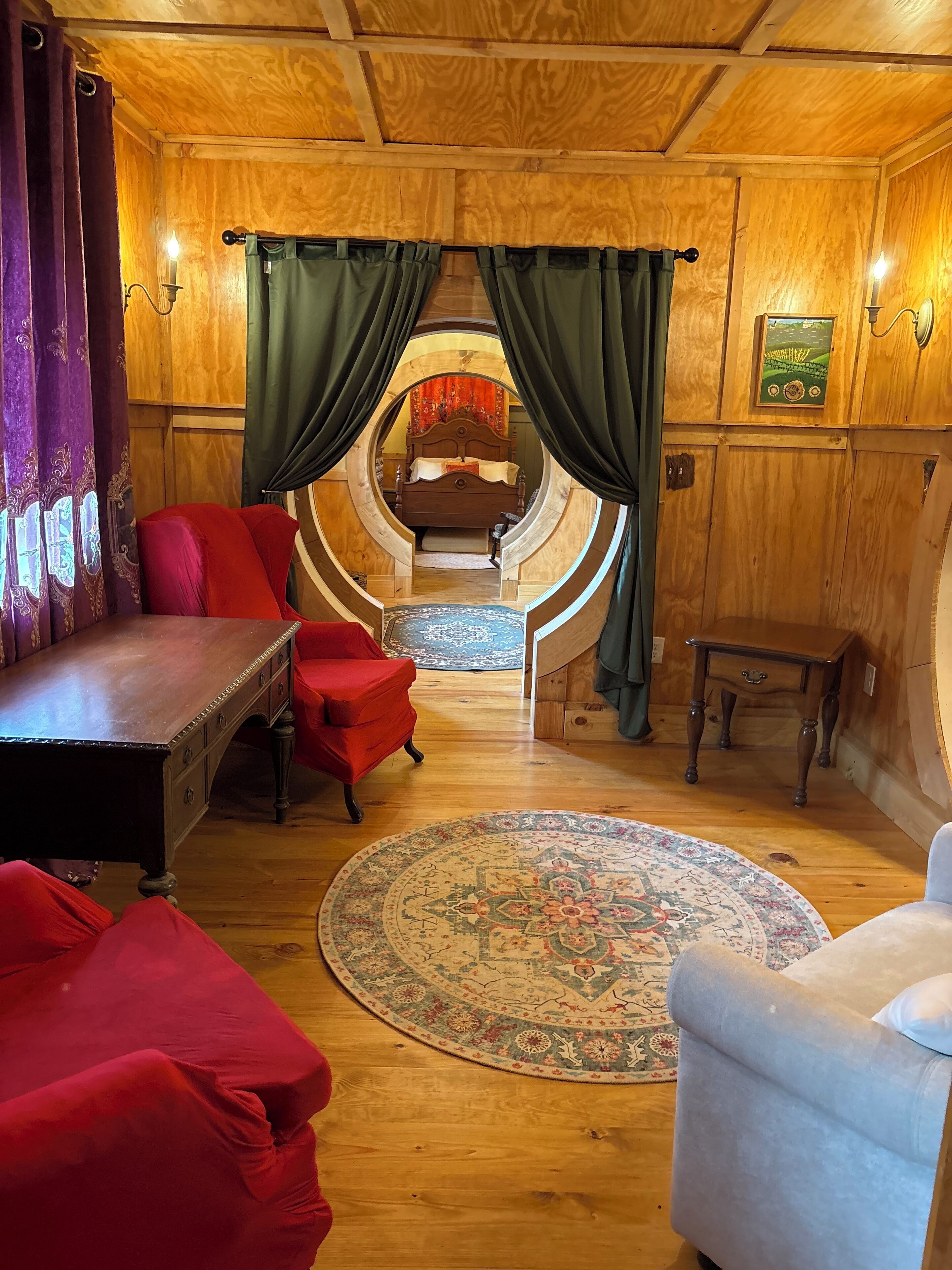 A circular room with a wooden ceiling, a bed with a headboard, a round rug, and a small table.