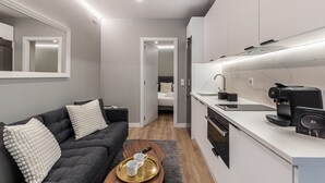 A modern, compact living space with a sofa, a small dining table, a kitchen area with a coffee machine, and a separate sleeping area. - Waou Essence IV Antón Martín - Corta Duración (Madrid)